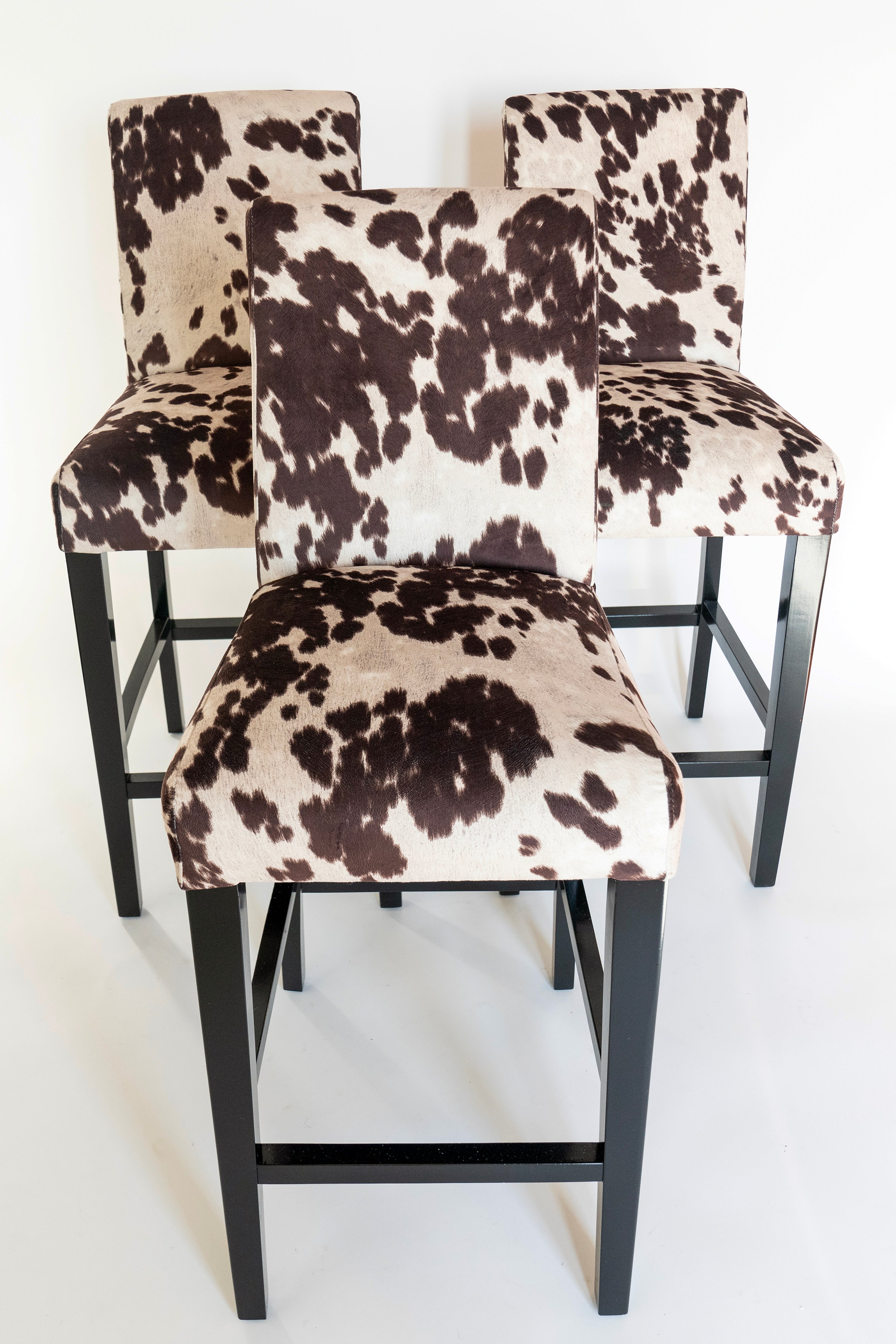 three bar or counter stools facing front with brown cow print fabric